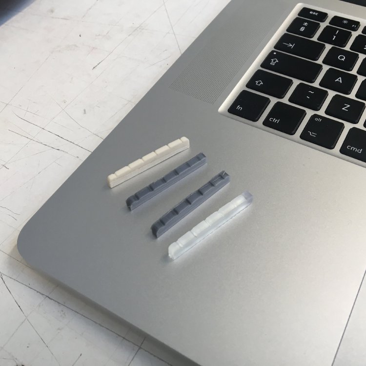A series of 3D-printed nuts in various materials (one white, two gray, and one clear), all balanced on a laptop.