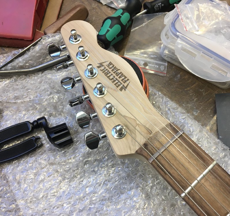 The closeup of a headstock of a finished guitar neck, with a clear 3D-printed nut.