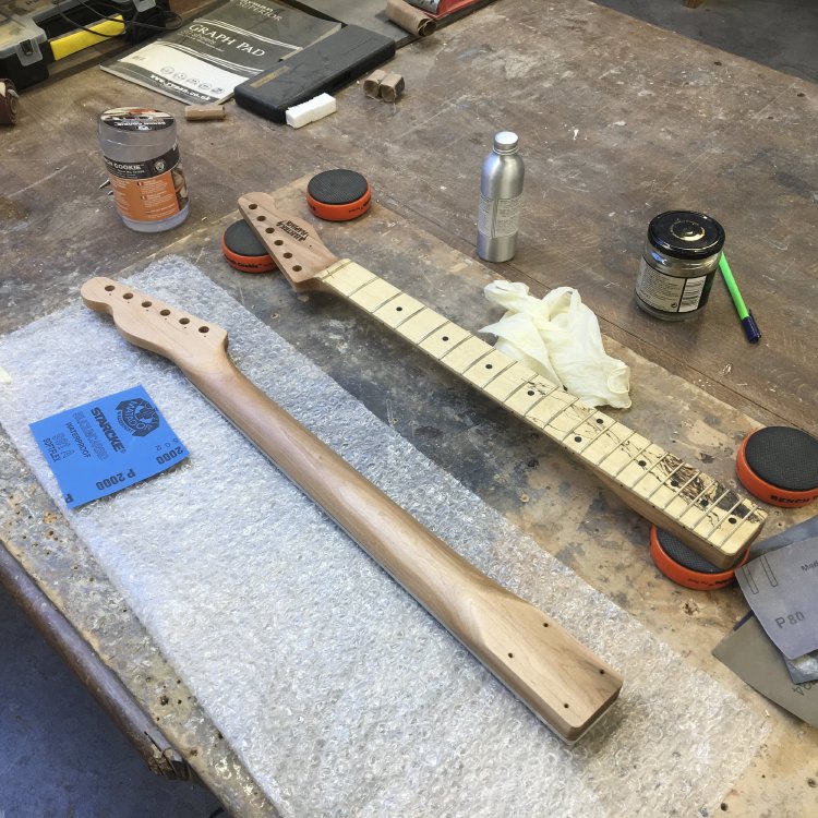 Two guitar necks sit of the workbench, one fretboard up, one fretboard down, and beside them sits some oil and a rag.