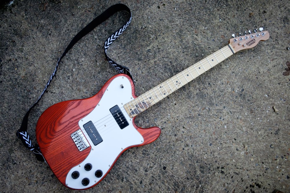 A photo of a finished electric guitar, stained orange with a pale wood fretboard and neck.