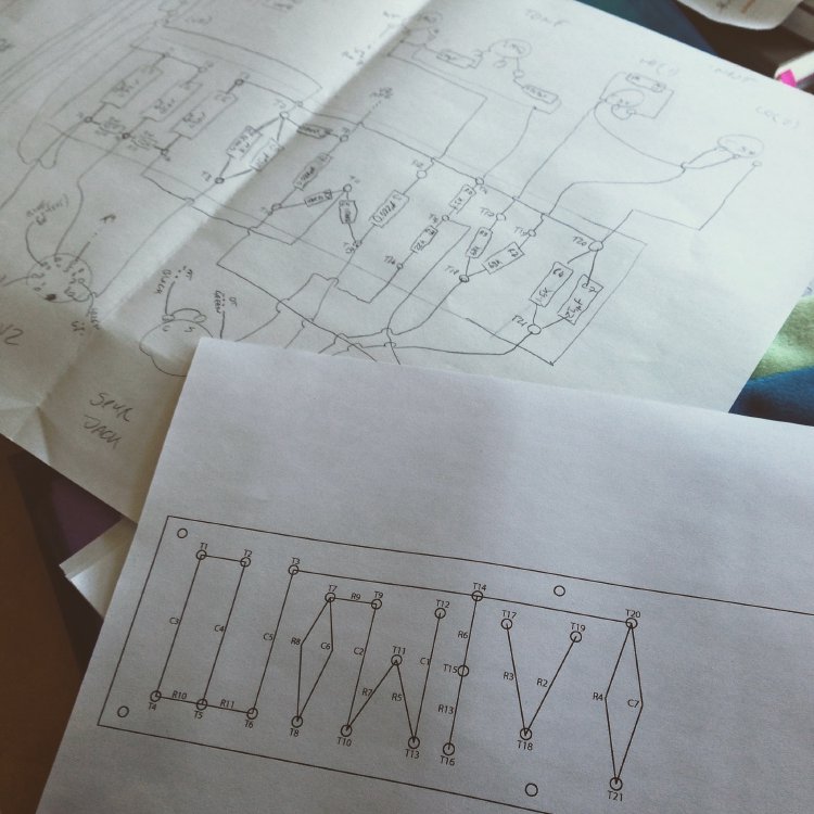 Bits of paper on a workbench, one of which is a hand drawn schematic for an amplifier, and the second is a printed schematic for the amp's turret board.