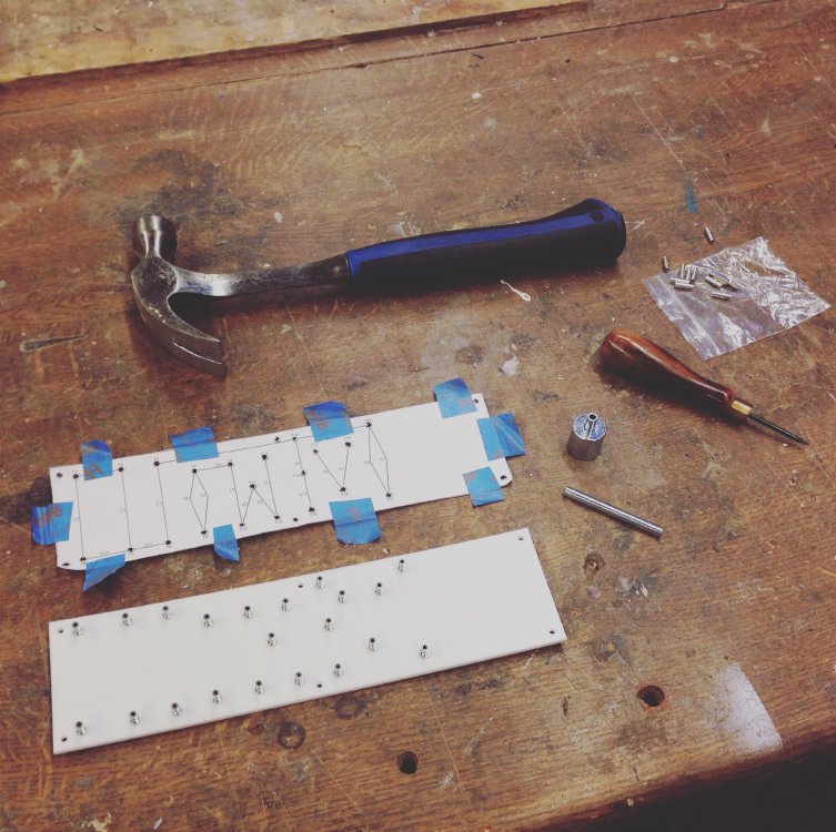 A photo of a workbench on which a turret board is being built. You can see the white insulating material board with some of the turrets in, a print out of the schematic, and a hammer and other tools used to embed the turrets in the board.