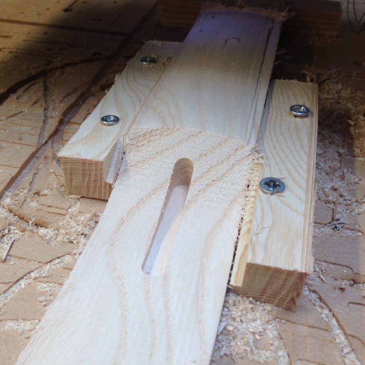A photo of a small block of wood on the bed of a CNC-router with the headstock to fretboard transition of a neck carved into it.