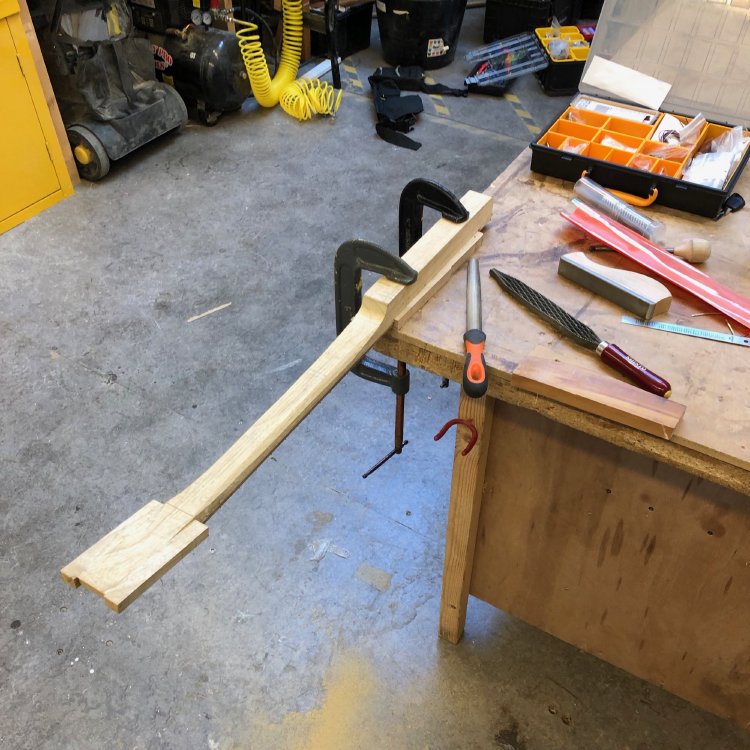 The neck is clamped one more to the workbench, but this time fretboard side down, with the rear of the neck being carved to a curve. Beside the neck on the workbench sit a set of rasps with different coarseness.