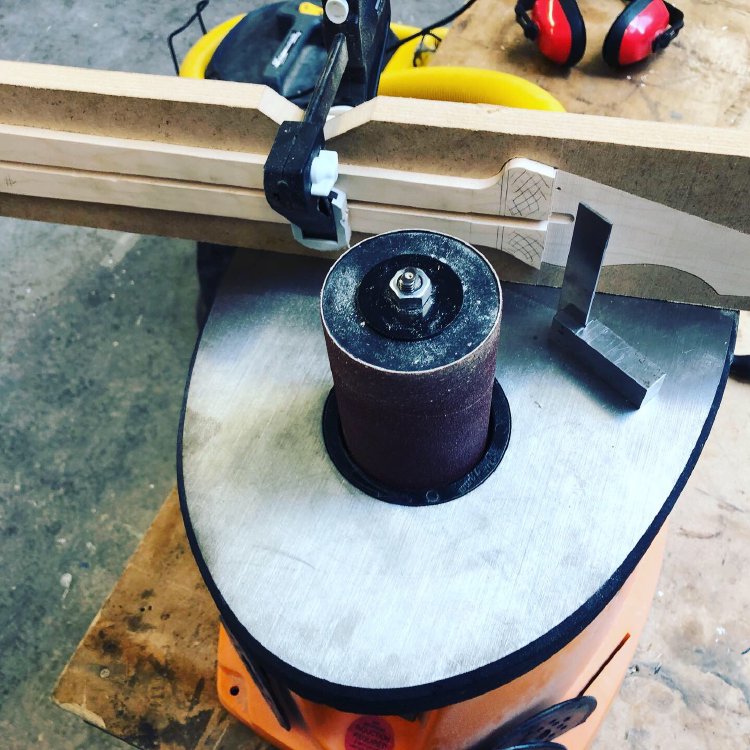 The neck in progress sits on the plate of a spindle-sander, waiting for the step left by the bandsaw process to be rounded out.