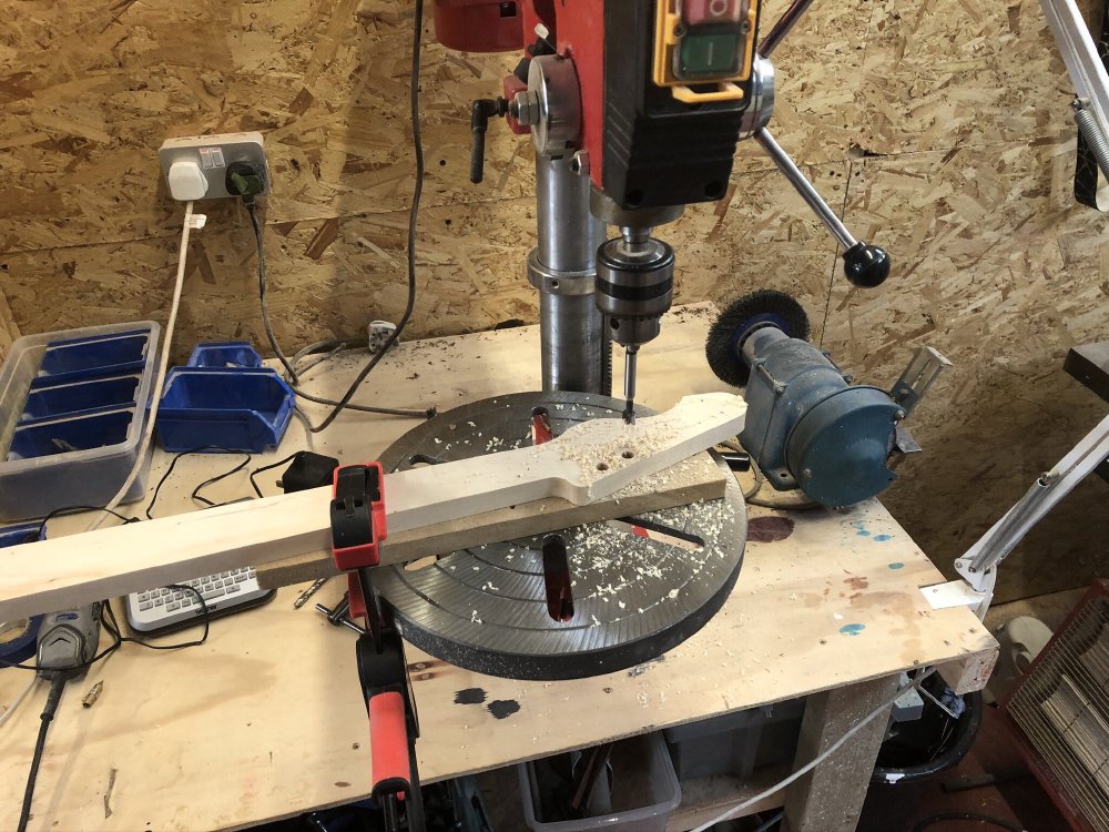 The roughly shaped guitar neck is on a pillar drill, with the holes for the tuning pegs being drilled.