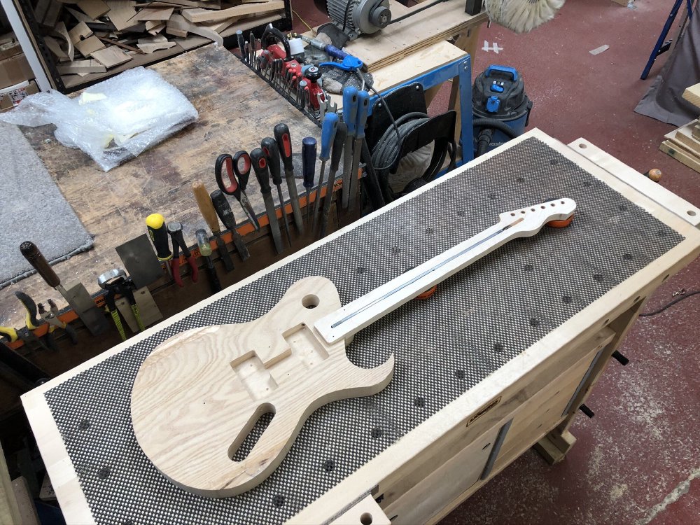 The work in progress guitar sits on the workbench, with the roughed out neck attached to the roughed out body.