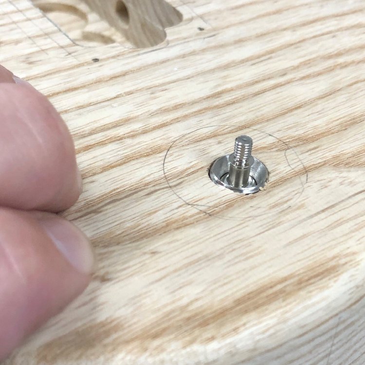 A close up of the top of the guitar body, where there is a small hole drilled for mounting the pickup selector switch. The switch is poking through, but not enough that the thread on the switch needed to mount it properly is visible.