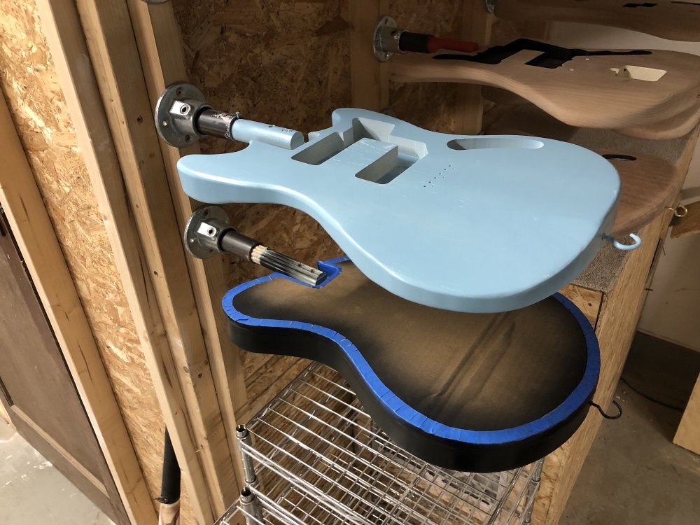 A photo of the two guitar bodies mounted on the wall to let the first coat dry off a bit. The mustang style one that was white in earlier photos is now a light blue, and the other still looks black as before.