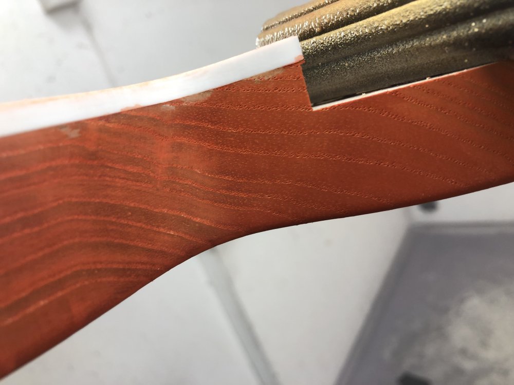 A close up on the side of the body, which is mostly stained orange, but you can see some unstained blotches under the plastic binding where glue has gotten into the wood and prevented the stain penetrating.