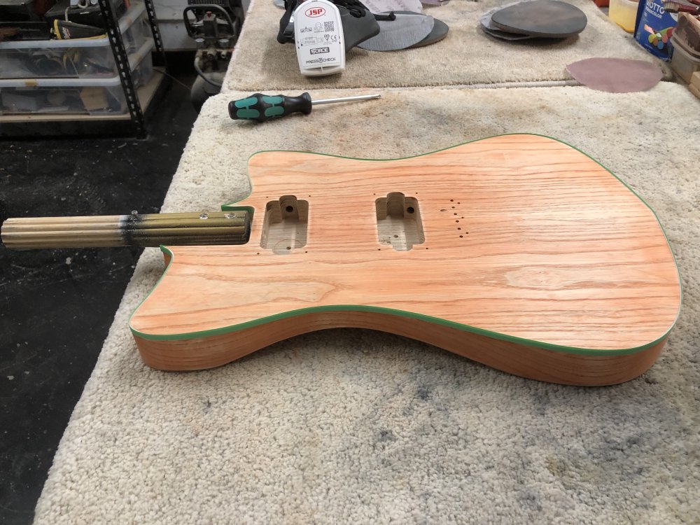 The guitar body back on the workbench as it started but now the wood is no longer a vivid orange, but a sort of pale peachy colour with more wood showing through in areas I've had to sand more.