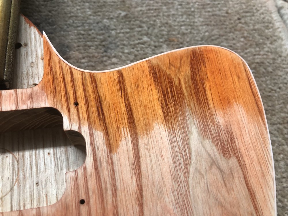 A similar photo to that first one, showing a section of the face of the guitar body with binding it, and this section has orange stain applied around the binding. The stain is mostly consistent, but is slightly less intense at the edge.