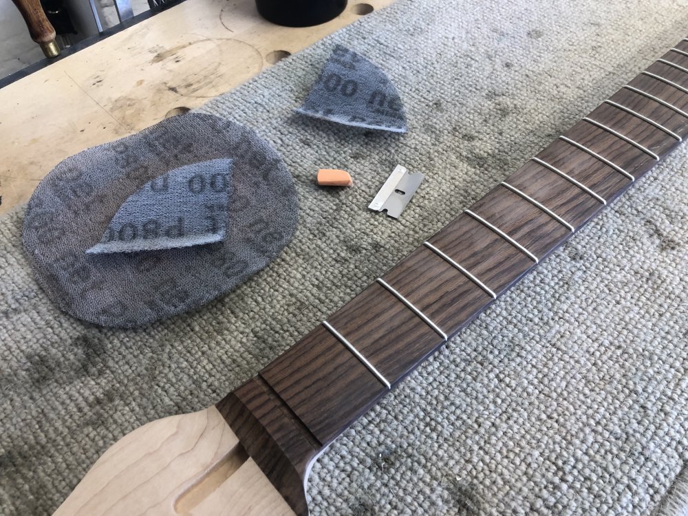 A photo of the guitar neck in question sat on a workbench, next to which lie sanding disks, chalk, and a razor blade.