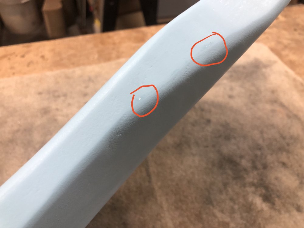A close up photo of the side of the guitar body where the belly-carve is. Circled in red are two spots where the blue paint has worn through to show the white primer layer.