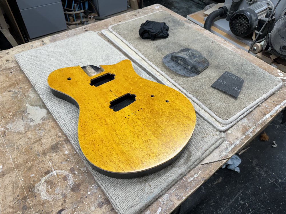 A photo of the yellow/black guitar body is on the workbench on a carpet mat to protect it from scratches. Next to it is a series of sanding pads.