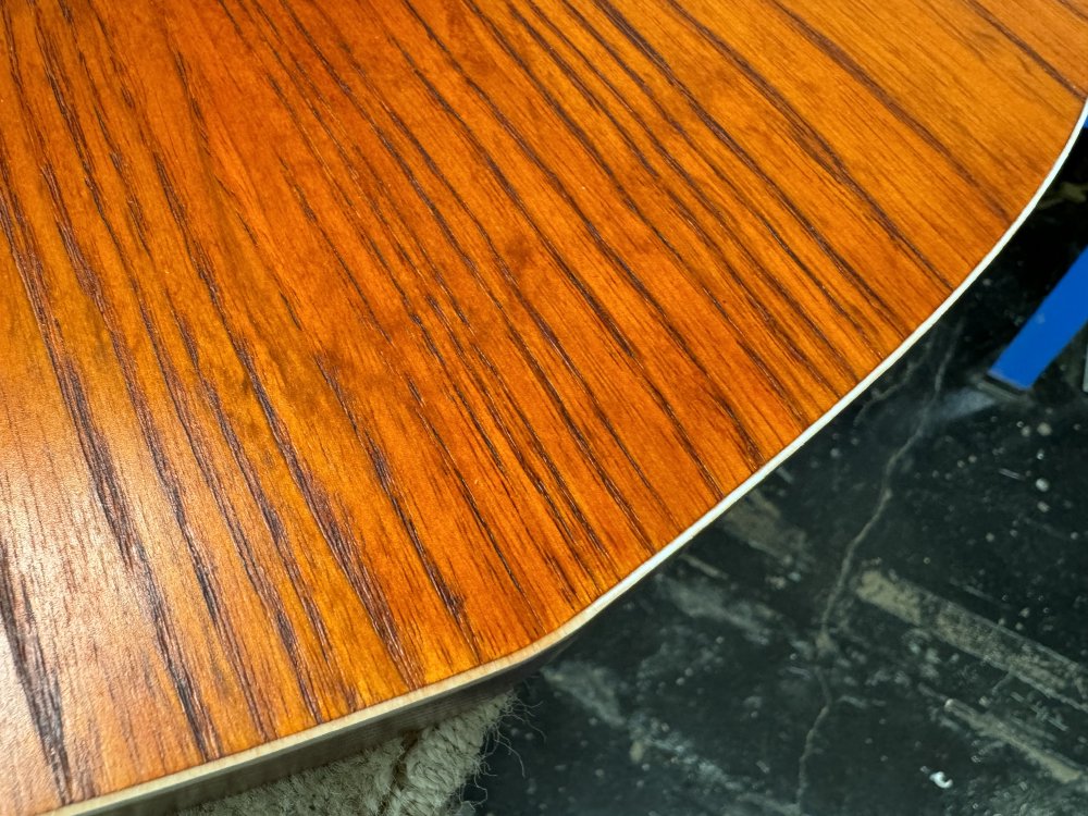 A close up shot of the guitar body with the binding. On one side you can see the binding, which should be white, has a slight orange stain on it due to the run off from staining the wood. On the other side you can see it's been cleaned to a bright white.