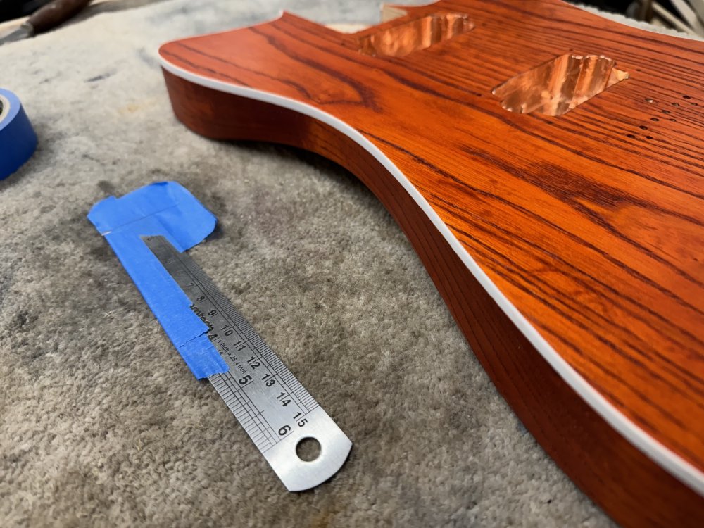 A shot of the guitar body on the workbench, with all the binding now looking bright white. Besides it is the metal ruler with a razor blade masking taped on.