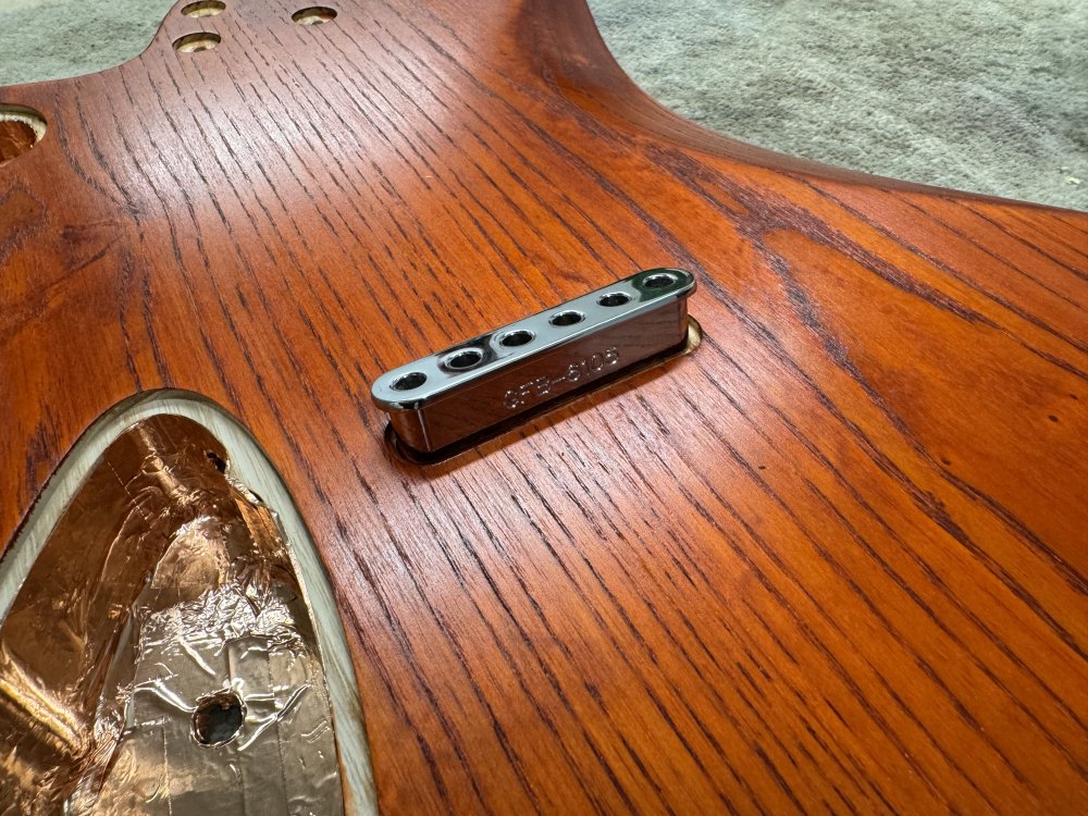 A photo of the back of the guitar body, showing a metal block with 6 holes in it (the string-ferrule block) resting over a hole into which is should fit, but it isn't.