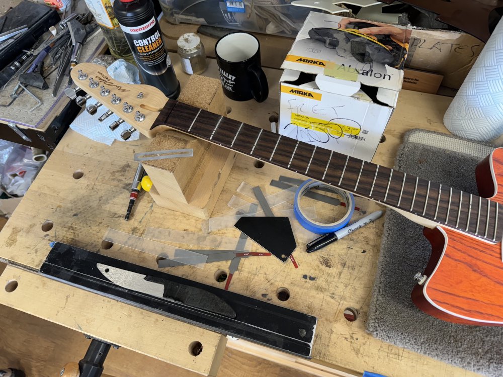 A photo of the guitar on the workbench, focussing on the neck. Around the neck sits an array of tools used for levelling and working on frets.