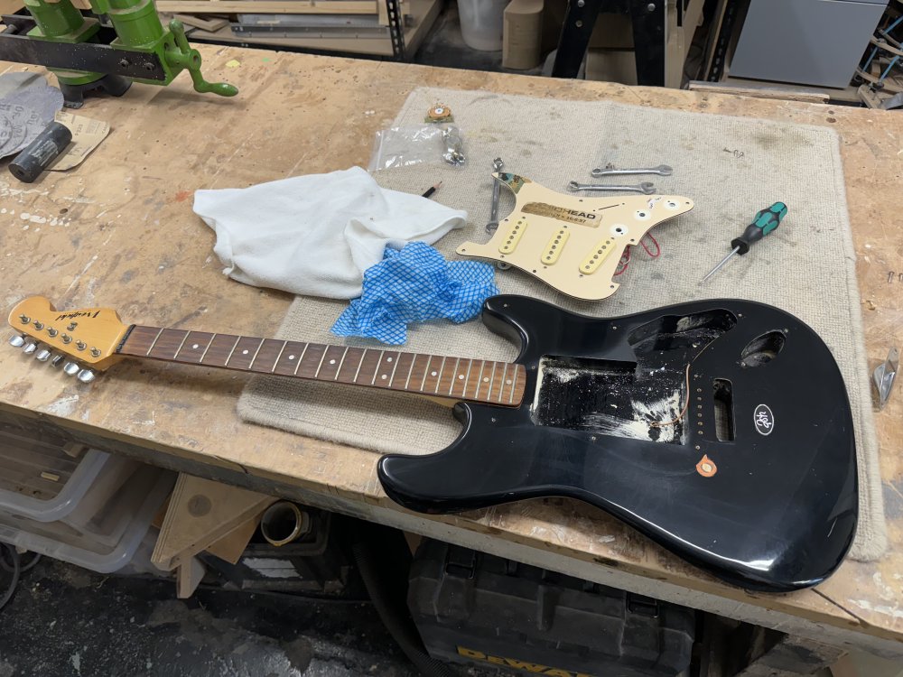 A photo of a classic-strat clone on a workbench, in parts and with some cleaning bits next to it.