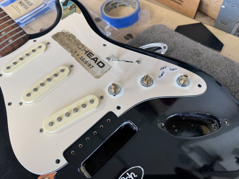 A photo of the pickguard sitting on the guitar body with the new pots and switch in place.