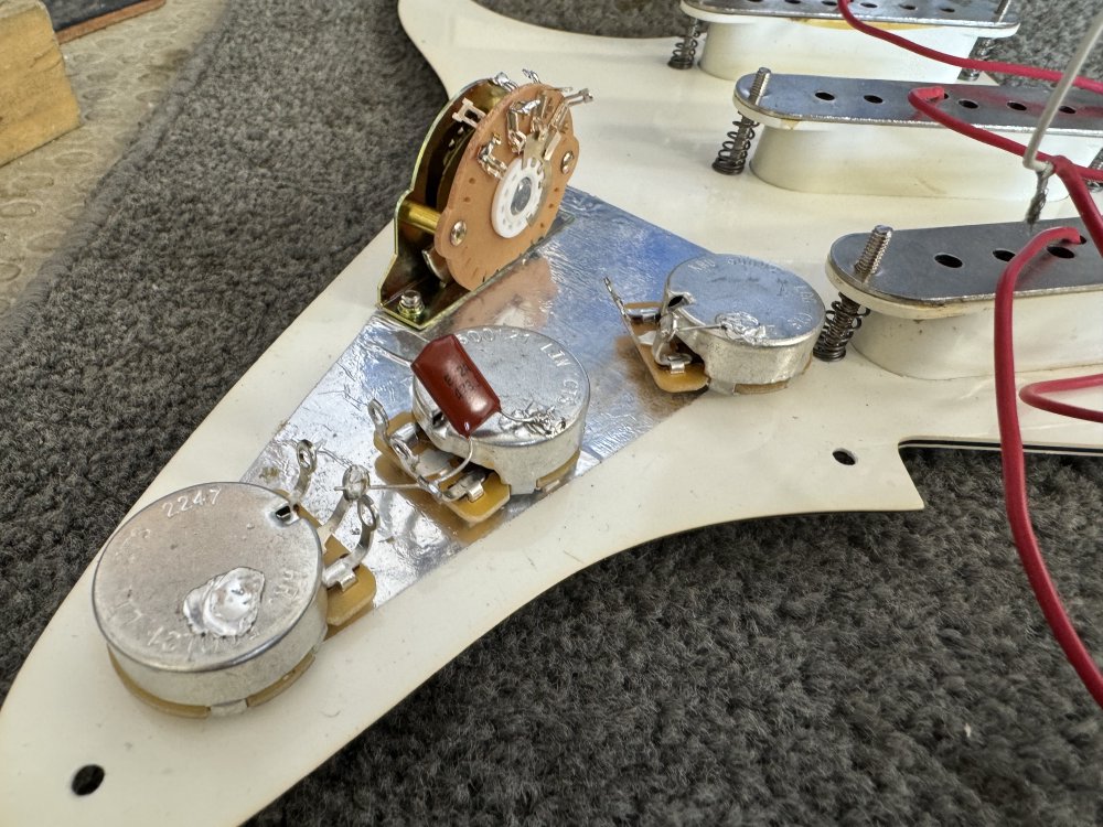 A photo of the backside of the pickguard with the pots mounted and a capacitor soldered into place between two of them.