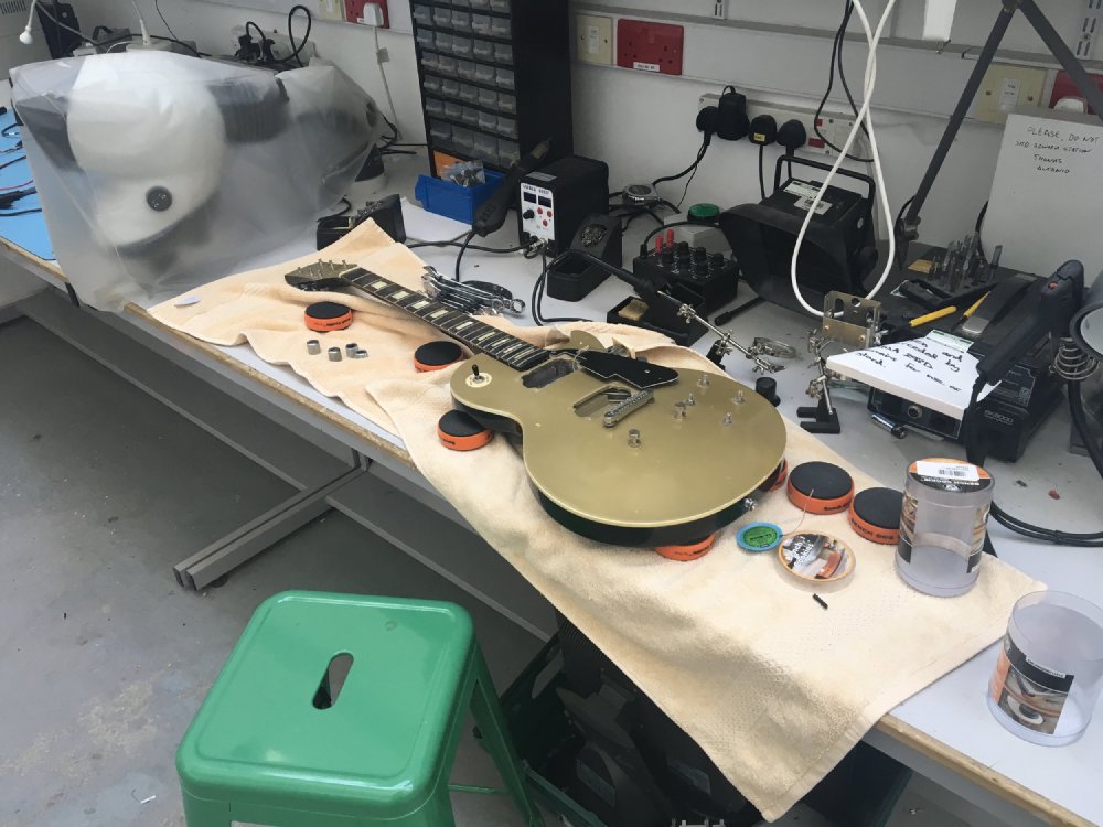 A gold topped Les Paul style guitar sites on the workbench with the electronics removed as part of a pickup replacement.