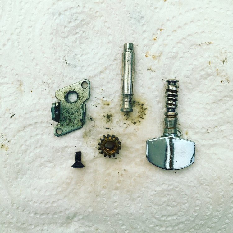 A disassembled machine-head/tuner sites on some kitchen roll as it is cleaned of gunk and old dirty oil.
