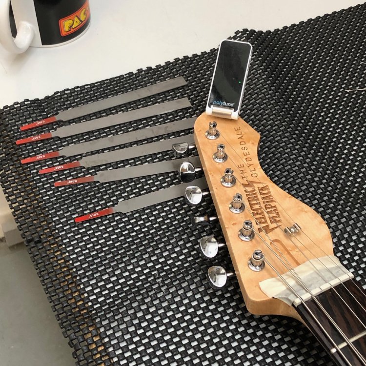 A close up of the headstock and nut of a guitar, with a set of nut files next to it, as the guitar gets a string setup.